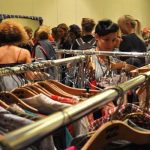 Rack of clothing with women in the background looking at clothing.