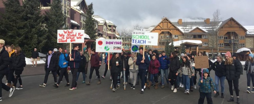 A big group of people walking down Whistler's village stroll, carrying signs about climate change and global warming, promoting environmental advocacy 