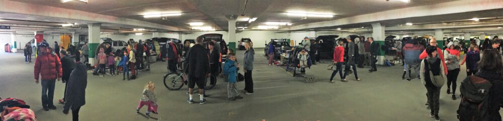 A group of people within an underground parking garage, wandering around looking at the vendors and their things for sale as part of the garage sale