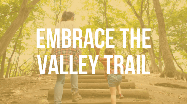 A graphic with text, the image is of two people walking, the text is "Embrace the valley trail"