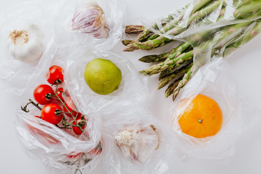 A variety of produce including tomatoes, asparagus, oranges, in plastic bags